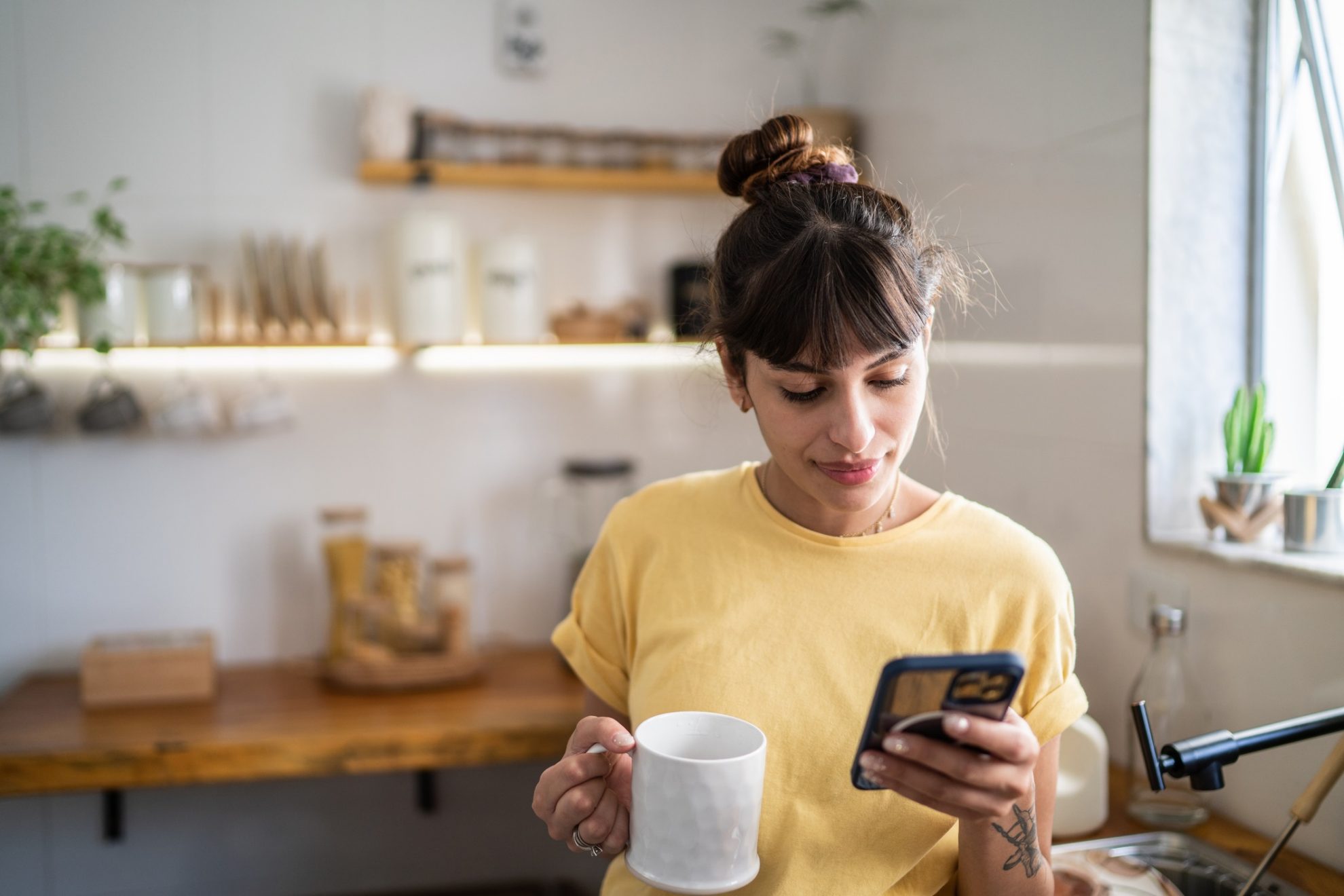 Young woman using the mobile phone while drinking coffee or tea at home