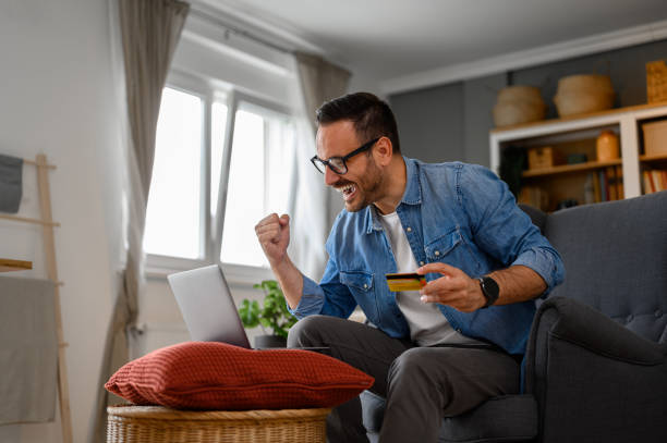 Businessman with credit card pumping fist and screaming in joy while doing online shopping on laptop